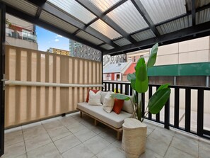 A balcony with a cushioned seating area, a potted plant, and a view of buildings. - Stylish 2-bed House Near Sydney CBD (Sydney)