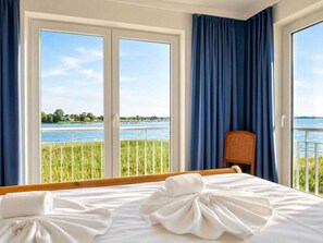 Ein Hotelzimmer mit Bett, einem Sessel und Blick auf einen See durch große Fenster.