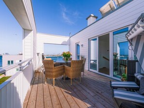 Eine Holzterrasse mit Korbmöbeln und einer Glastür, die auf einen Balkon mit Meerblick führt.