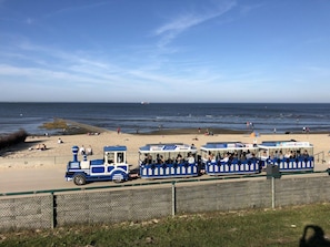 A seaside train with passengers, a beach in the background, and a clear sky. - Finkennest - Pavilion (Cuxhaven)