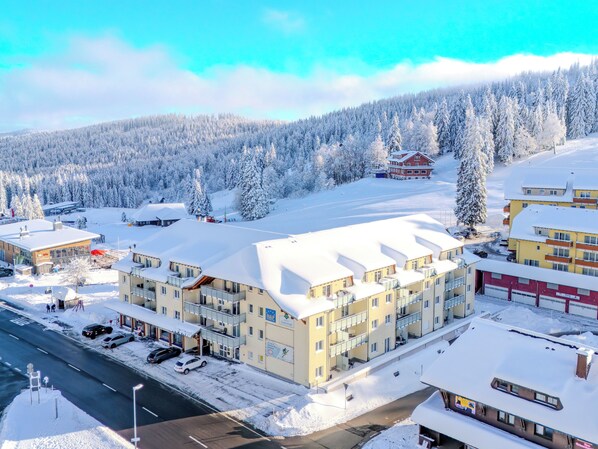 Ein Hotel mit mehreren Etagen, einem Parkplatz und Blick auf einen verschneiten Wald.