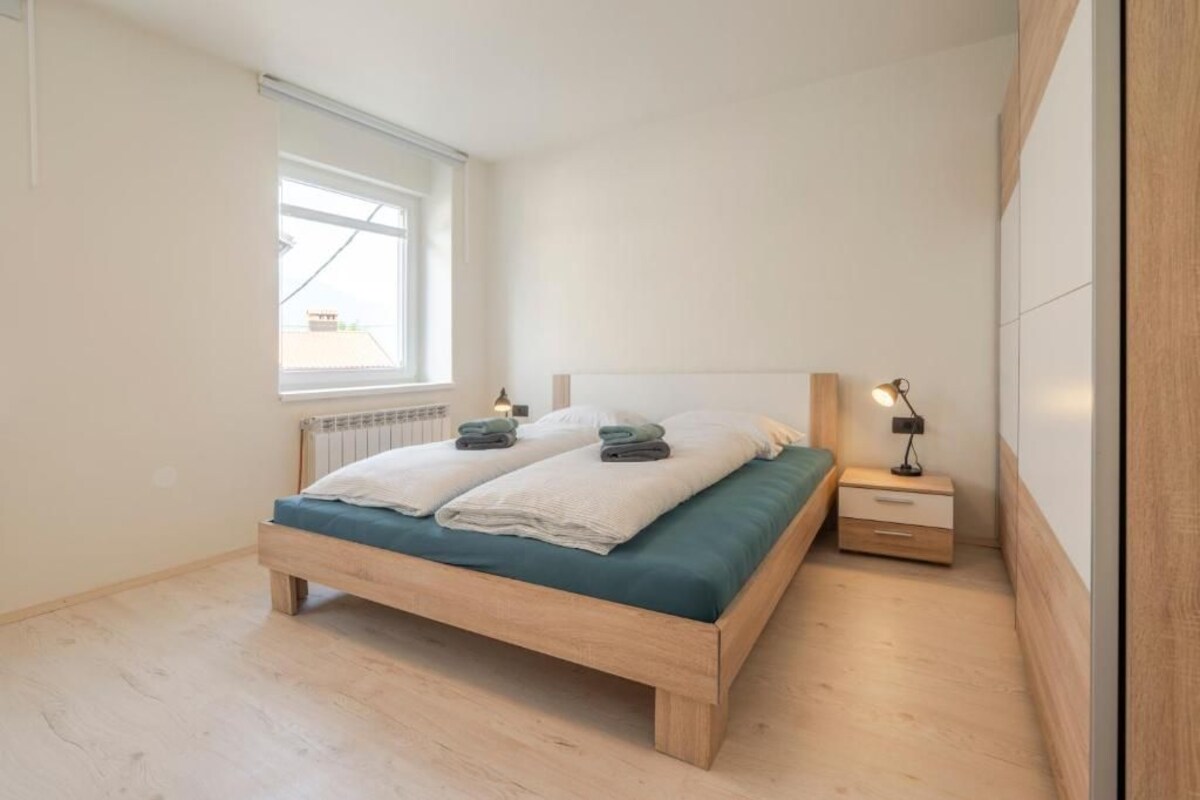 A bedroom with a wooden bed, a nightstand, a lamp, and a window.
