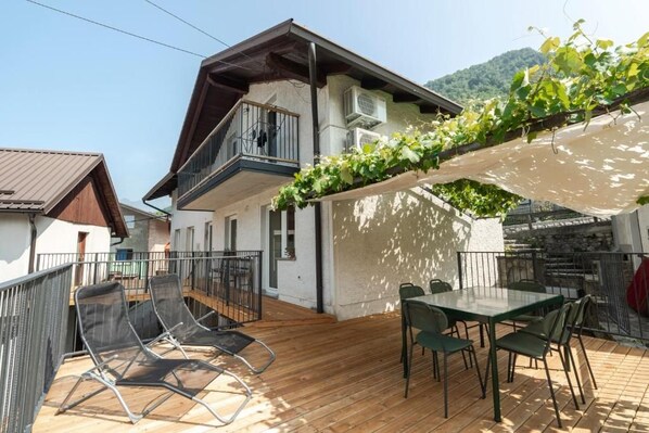A balcony with a table and chairs, a wooden deck, and a house with a balcony. - Holiday Home Lukc (Kobarid)