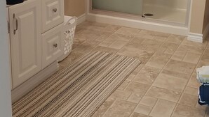 Un baño con ducha, lavamanos, toallero y alfombra estampada.