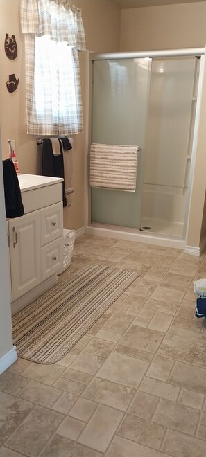 Un baño con ducha, lavamanos, toallero y alfombra estampada.