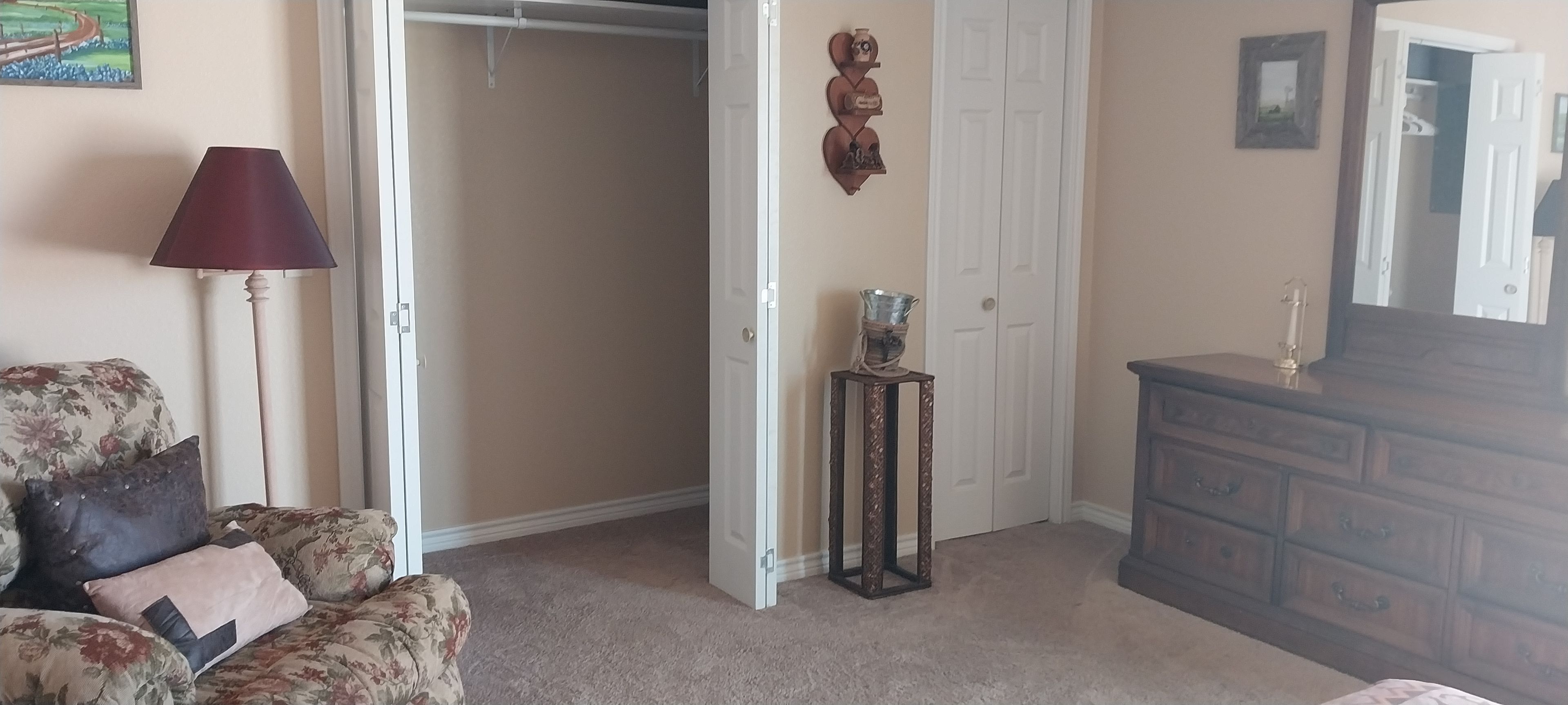 Une pièce avec un canapé à motifs floraux, une commode en bois, un miroir et une porte donnant sur une autre pièce.