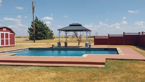 Una piscina rectangular con un pabellón en el centro, rodeada por una cerca roja y un edificio rojo con una puerta blanca.