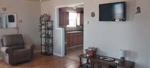 A living room with a brown leather sofa, a wooden coffee table, and a television mounted on the wall.