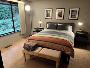 Un dormitorio con una cama grande, lámparas de noche, un banco y cuadros en la pared.