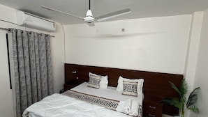 A hotel room with a bed, a ceiling fan, a potted plant, and a window with curtains. - Classic Ayodhya Junction Road (Faizabad)