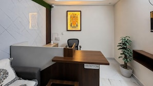 A reception desk with a sign, a framed picture on the wall, a potted plant, and a modern chair. - Classic Ayodhya Junction Road (Faizabad)