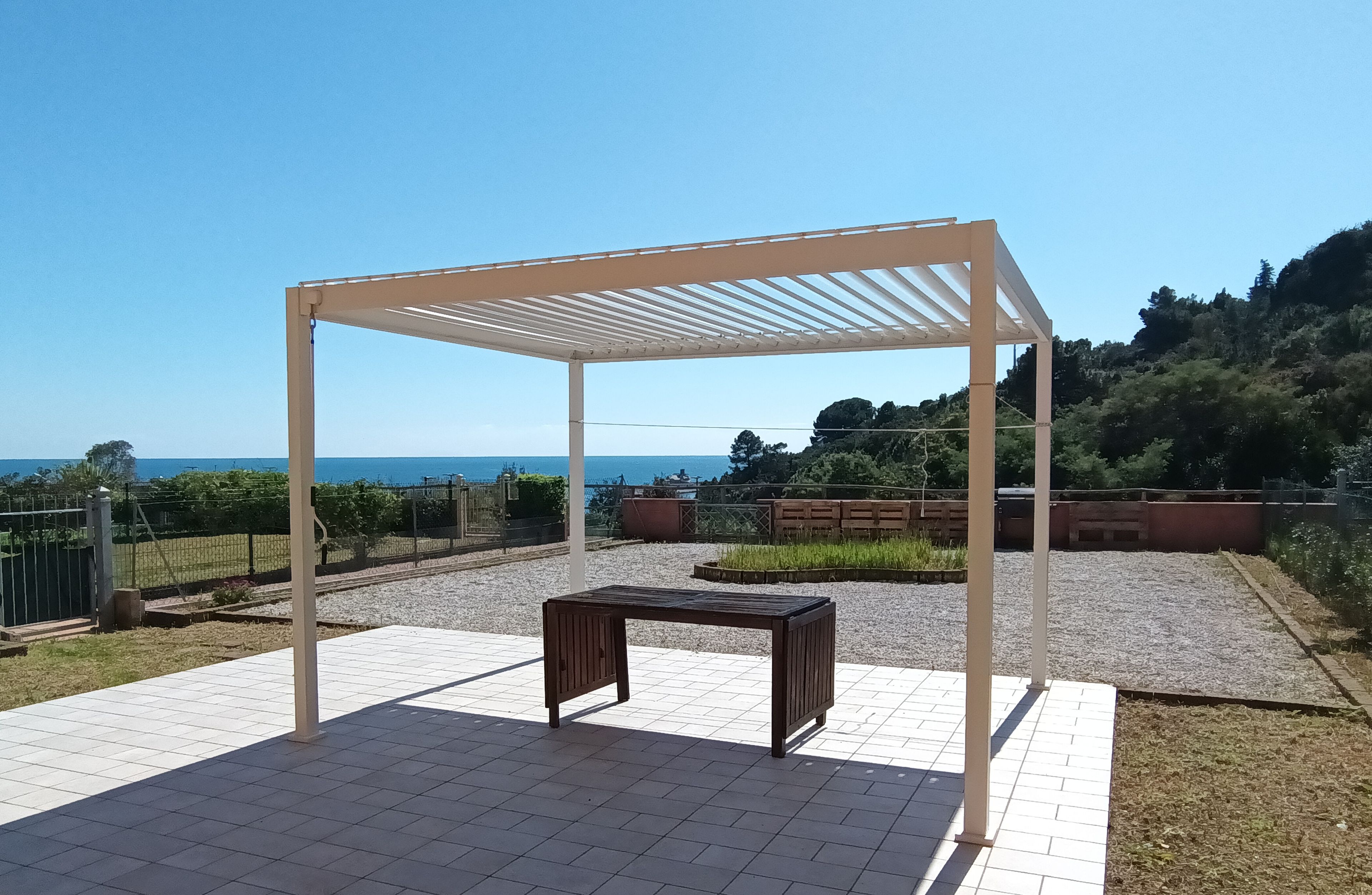 A covered outdoor area with a pergola, a small table, and a view of the sea.