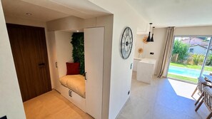 A modern interior with a sliding door leading to a balcony, a bed with a red pillow, a wall clock, and a view of a swimming pool. - New villa for 6 people - Pool - Beach 800 m away (Fréjus)
