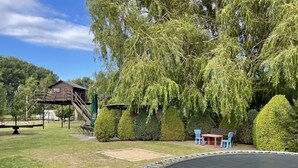 Ein Spielplatz mit Trampolin, Holzspielhaus und Schaukeln.
