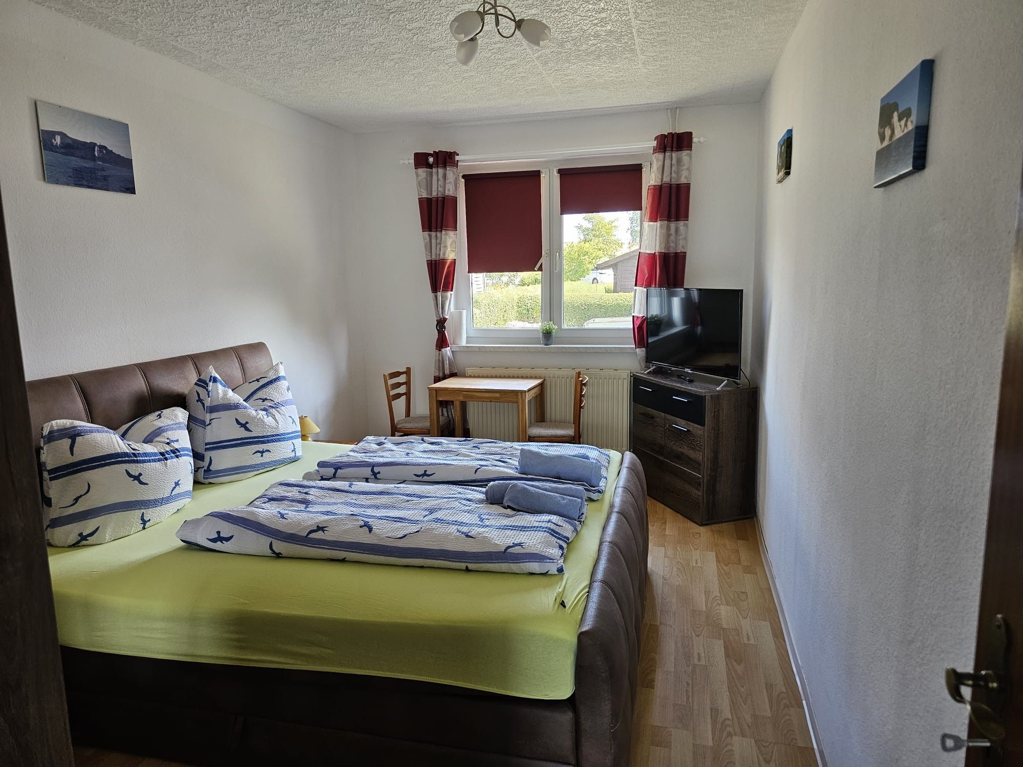 Ein Schlafzimmer mit einem Bett, einem Schreibtisch, einem Sessel, einem Fernseher und einem Fenster mit Vorhängen.