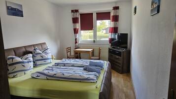 Ein Schlafzimmer mit einem Bett, einem Schreibtisch, einem Sessel, einem Fernseher und einem Fenster mit Vorhängen.