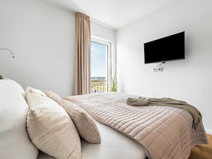Un dormitorio con una cama, un televisor montado en la pared y un ventanal con cortinas.