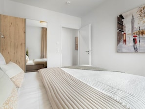 Habitación de hotel con una cama grande, un revestimiento de madera en la pared, una puerta que conduce a otra habitación y un cuadro que muestra a una pareja en una calle lluviosa.