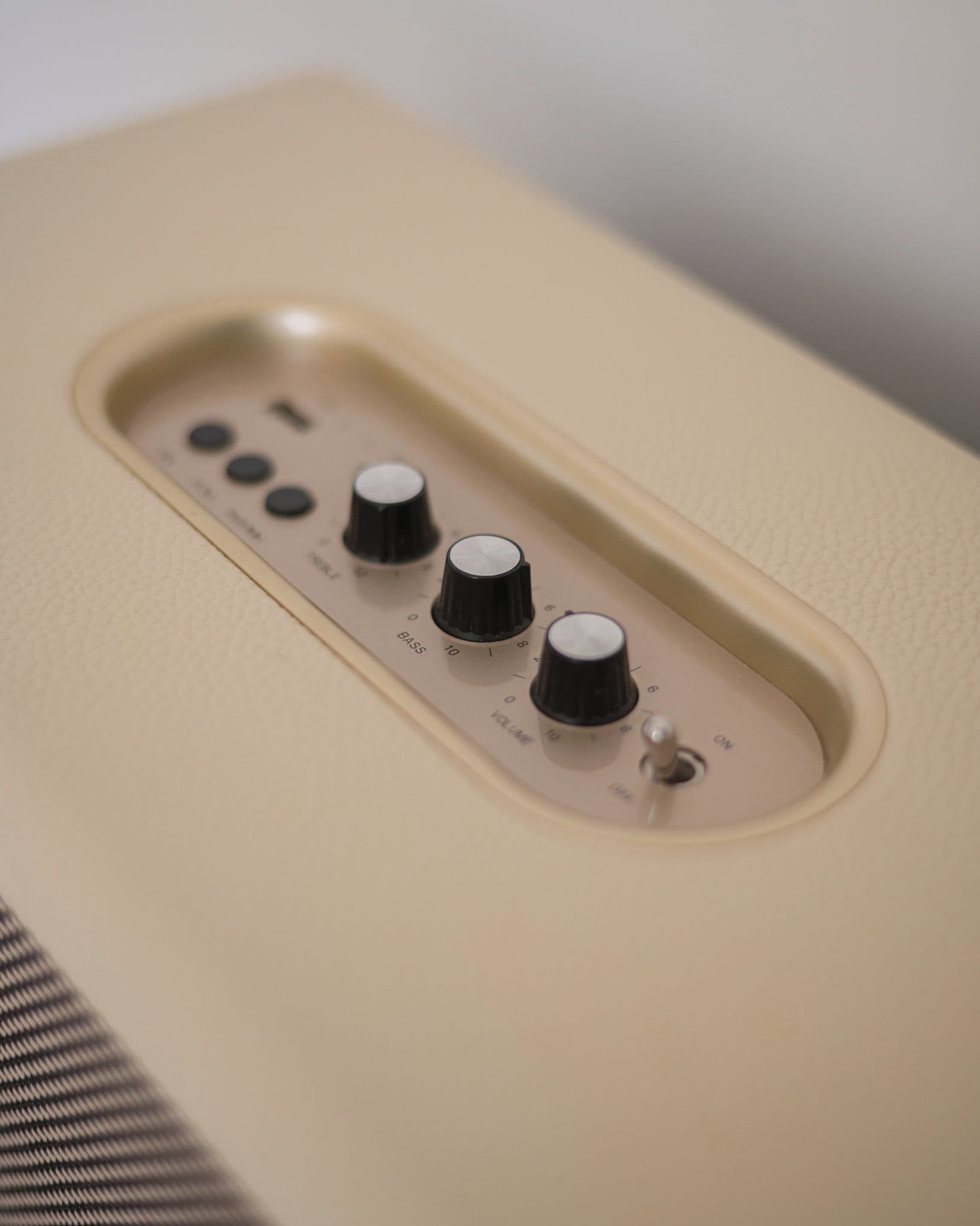 Un altavoz beige con cuatro perillas, una etiquetada 'VOLUMEN' y otra 'BASS'.