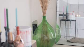 A room with a green vase containing dried plants, a white container, and a mirror reflecting a tiled wall and a table with candles.