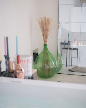 A room with a green vase containing dried plants, a white container, and a mirror reflecting a tiled wall and a table with candles. - VICOLOTERZO SUITE (Bari)