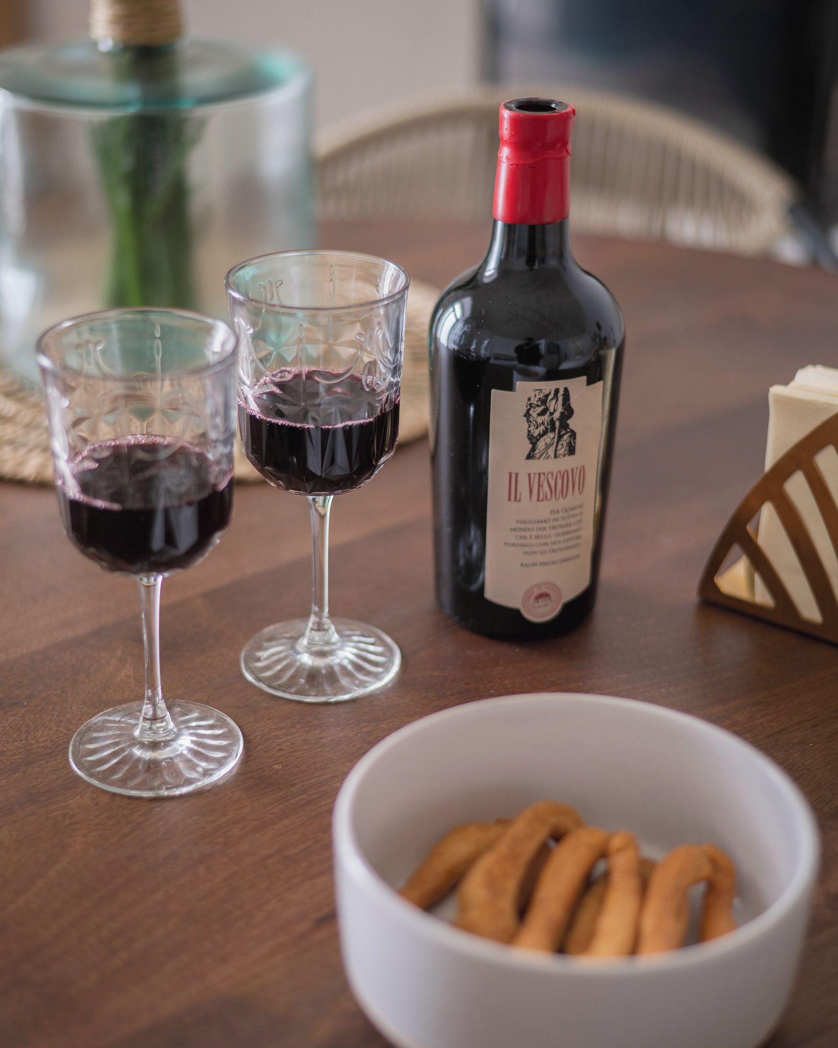 Una mesa con dos copas de vino, una botella y un bol de palitos de pretzel.