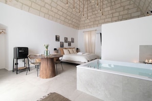 A modern bedroom with a large bed, a sitting area with a table and chairs, a bathtub, and a brick ceiling. - VICOLOTERZO SUITE (Bari)