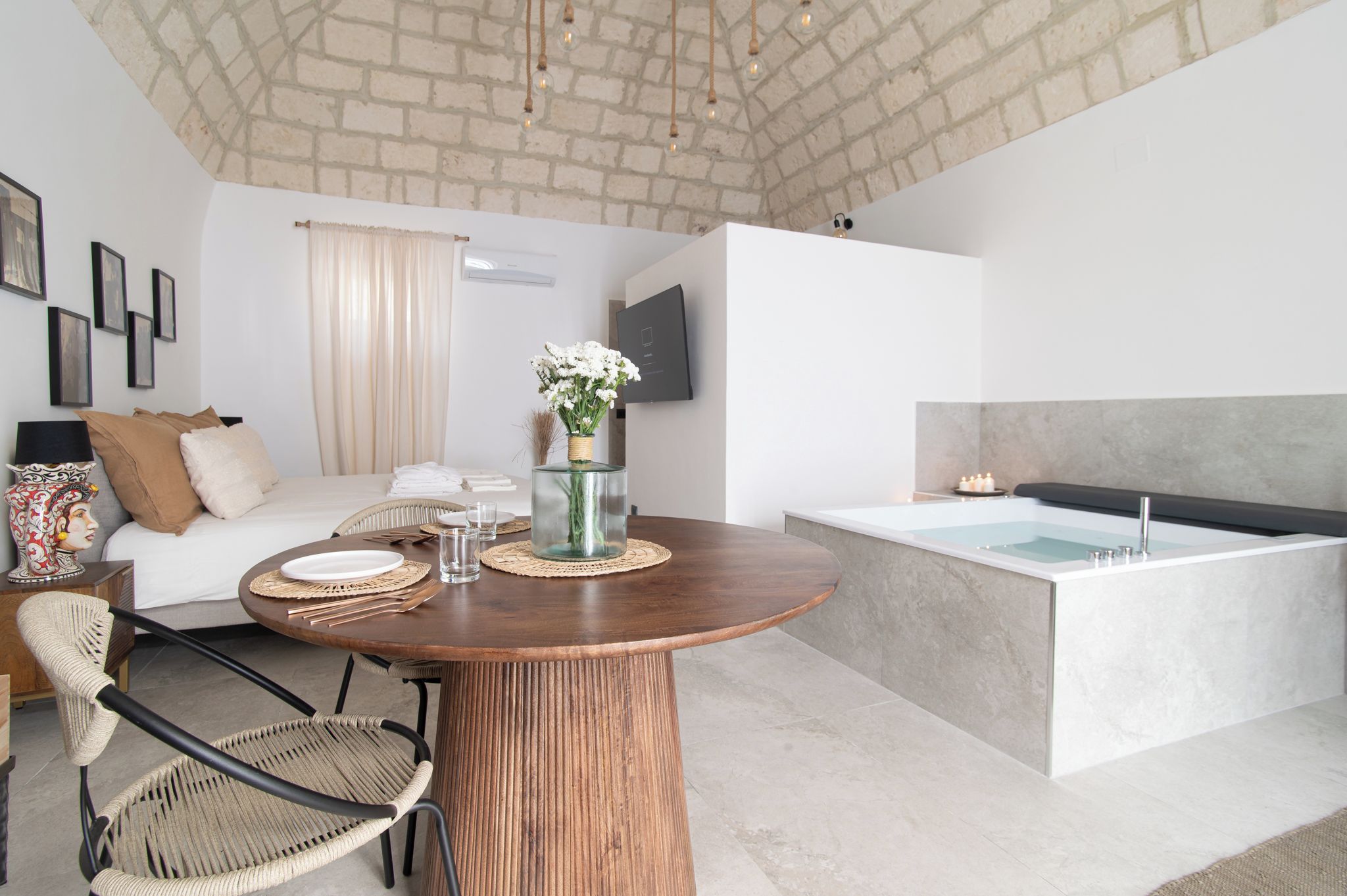 Una habitación de hotel moderna con zona de comedor, cama, televisor y bañera.