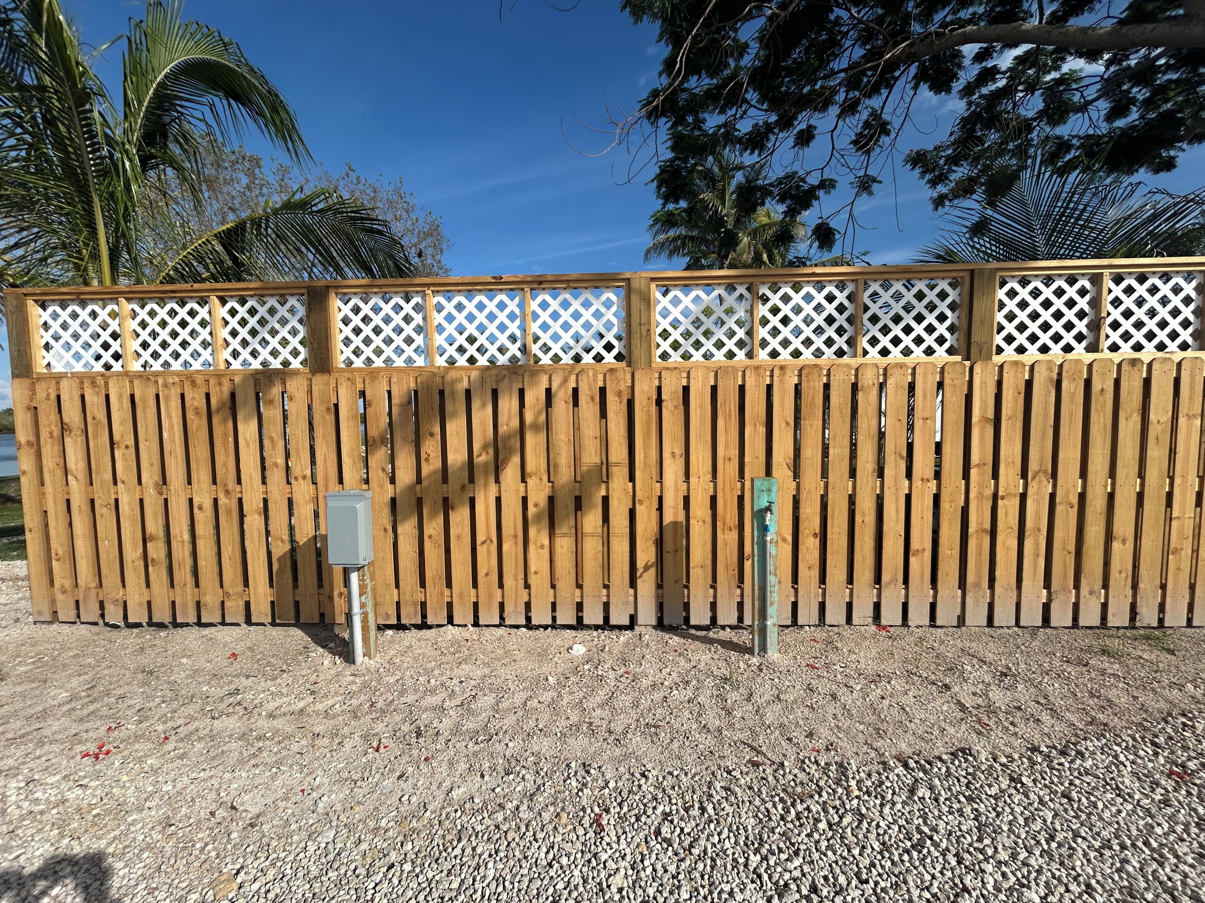 A wooden fence with a lattice top, a metal utility box, and a water spigot.