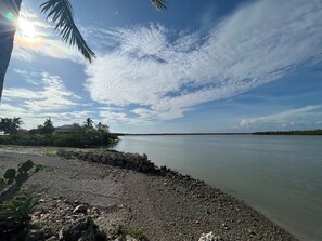 A calm body of water with a rocky shoreline, palm trees, and a clear sky. - Waterfront RV Site • Bring Your Own RV (Goodland)