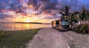 A truck parked by a dirt path with a body of water and palm trees in the background. - Waterfront RV Site • Bring Your Own RV (Goodland)