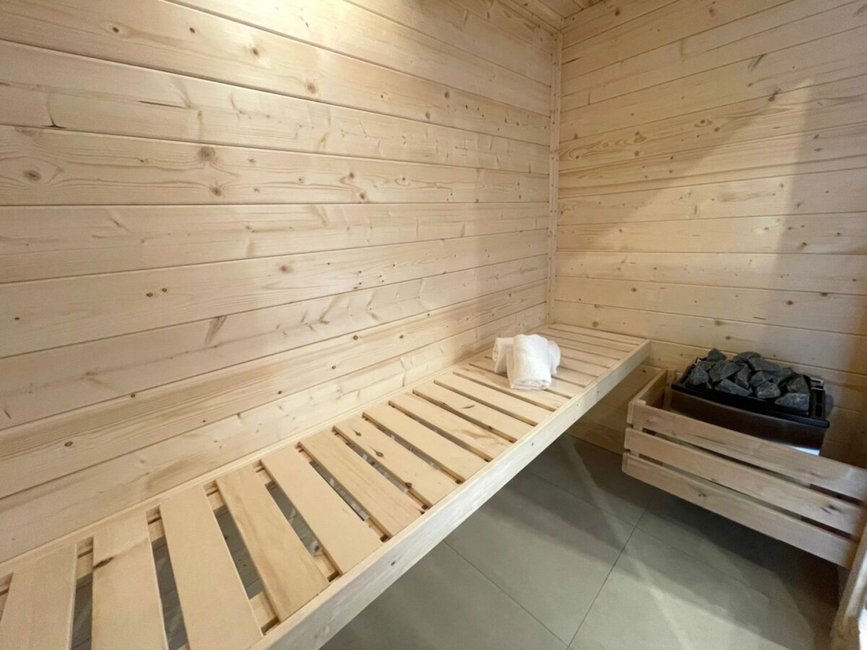 A sauna room with wooden walls, a bench, and a stone heater.