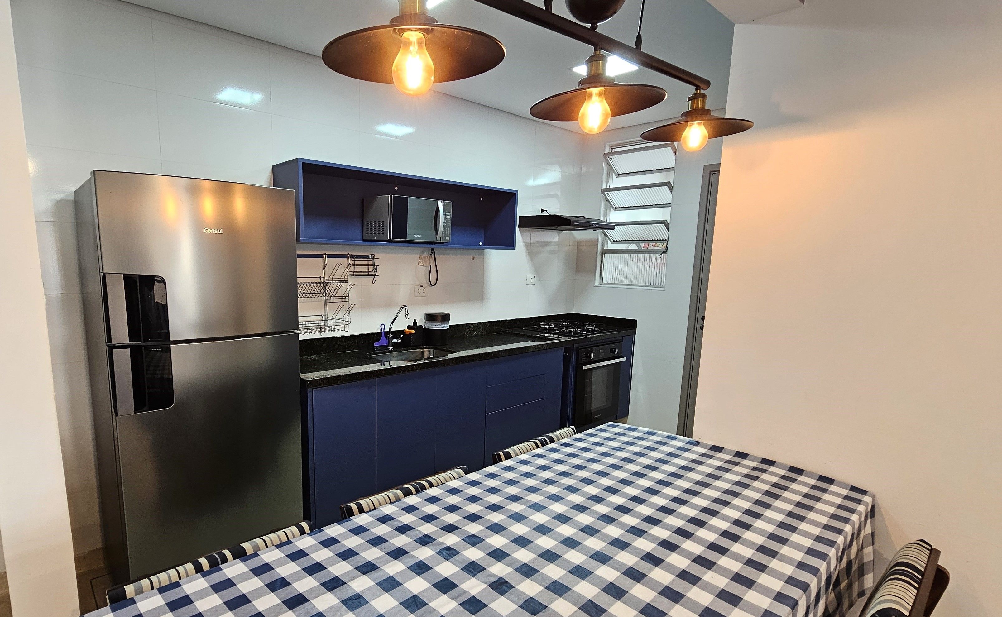 A compact kitchen with a refrigerator, microwave, and stove, a blue cabinet, and a checkered tablecloth.