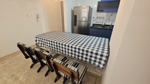 A compact room with a bed, a small table, two chairs, a refrigerator, and a kitchenette area. - Good Location | Pitangueiras Beach | Wi-fi (Guarujá)