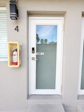 A door with a frosted glass panel, a fire extinguisher mounted on the wall, and a smoke detector installed above the door. - Miami MiMo Studio with Private Outdoor Area (Miami)