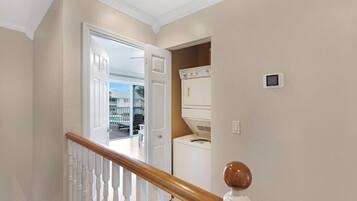 A laundry room with a washer and dryer, a thermostat, and a view of a pool through an open door.