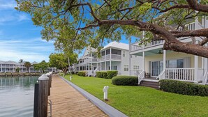 A waterfront property with a wooden dock, white buildings with balconies, and a clear sky. - Villa 7079 on Duck Key - Boat Slip Available (Marathon)