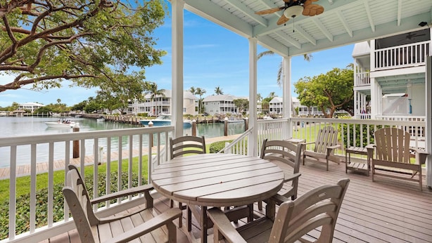 A covered outdoor area with a table and chairs, overlooking a body of water with boats and a dock. - Villa 7079 on Duck Key - Boat Slip Available (Marathon)
