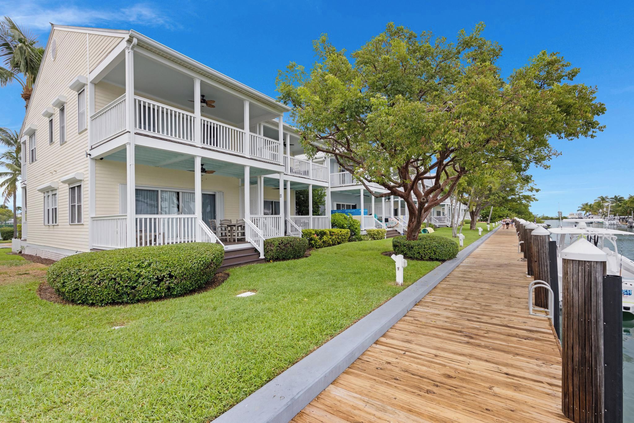 A multi-story hotel with a wooden deck leading to the water, surrounded by well-maintained lawns and trees.