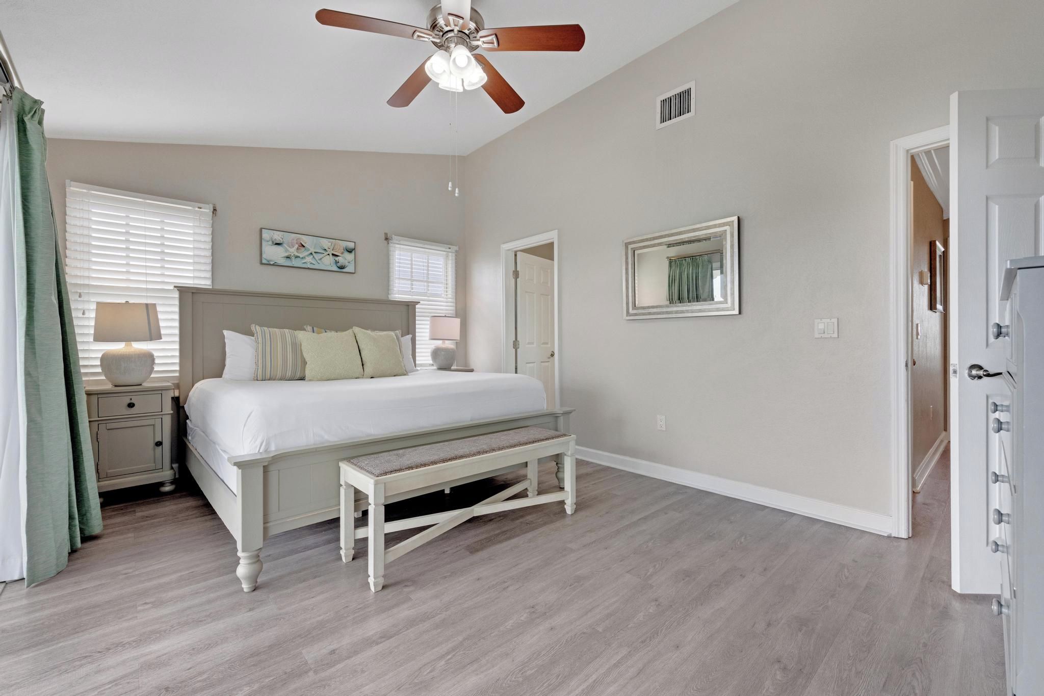 A bedroom with a bed, bedside tables, a bench, a ceiling fan, and a door.