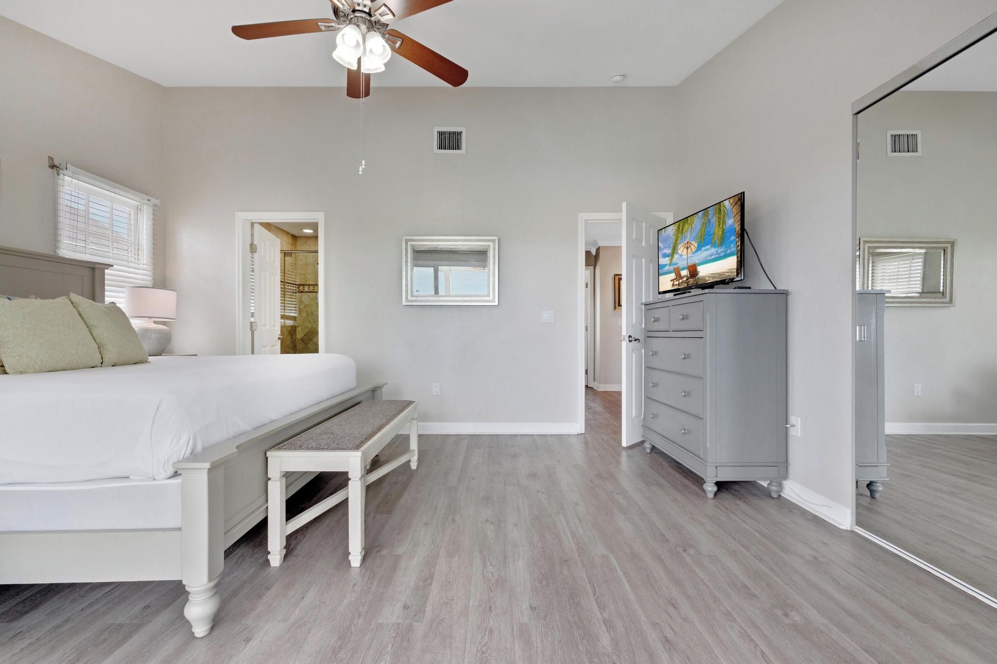A bedroom with a bed, a bench, a dresser, a ceiling fan, and a television.