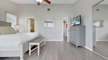 A bedroom with a bed, a bench, a dresser, a ceiling fan, and a television.