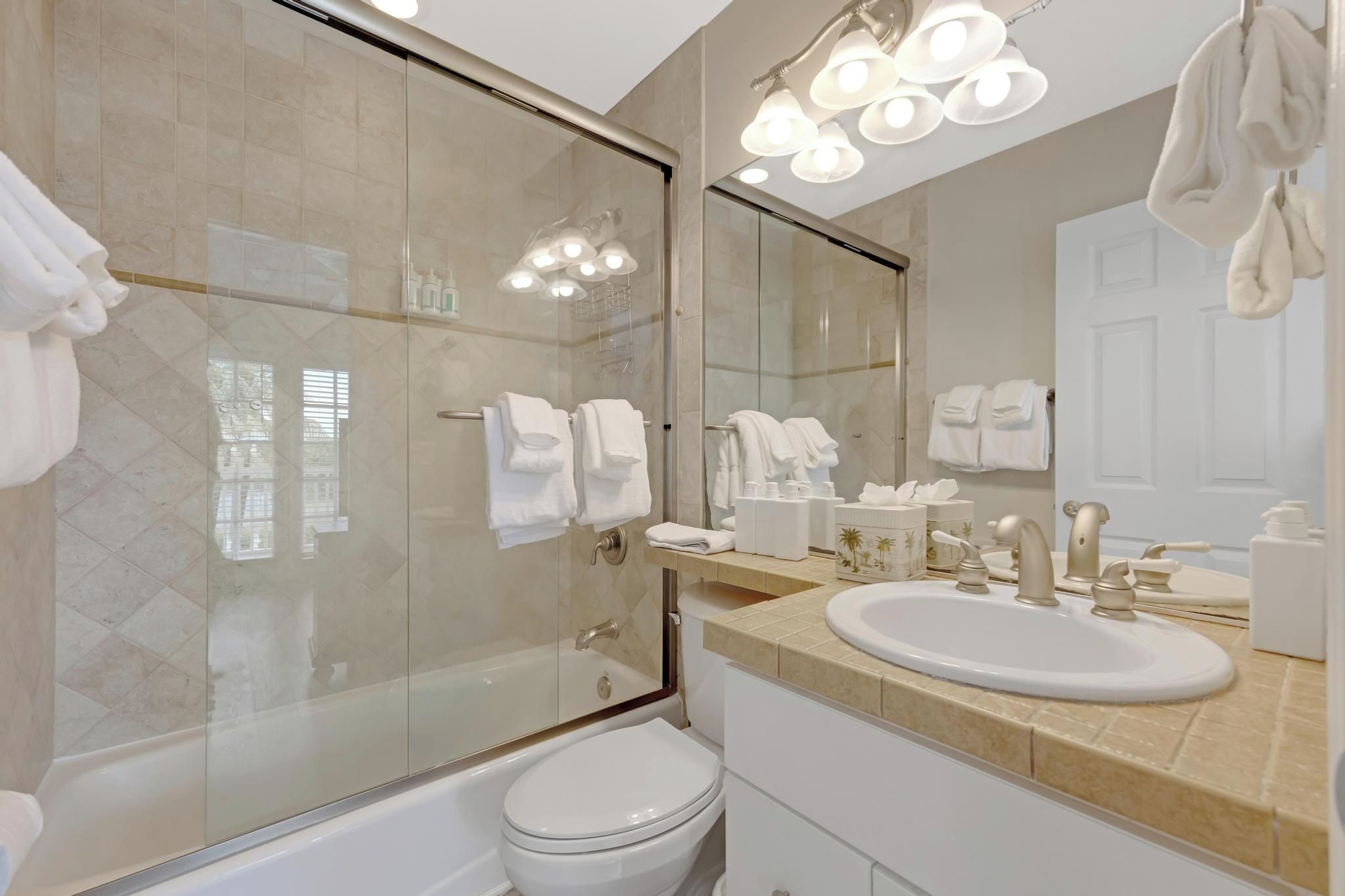 A modern bathroom with a glass shower enclosure, a white toilet, a sink with a vanity, and a large mirror.