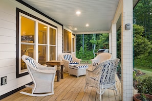 Ein überdachter Balkon mit Korbstühlen und einem Grill, mit Blick auf einen Garten.