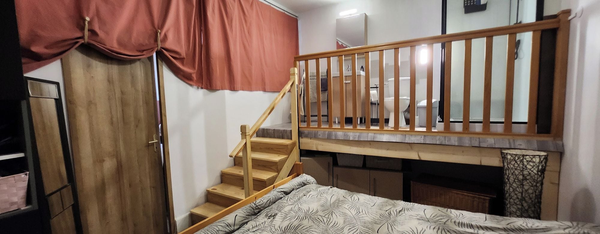 A bedroom with a bunk bed, a wooden staircase, and a red curtain.