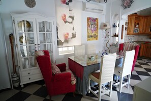 Een eetgedeelte met een tafel met glazen blad, rode fauteuils, een wit kastje met glazen deuren, en een keuken op de achtergrond.