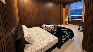A bedroom with a bed, a window with curtains, and a view of mountains. - DORJE HILL STAY DARJEELING - KANCHENJUNGA VIEW COZY HOMESTAY (Darjeeling)