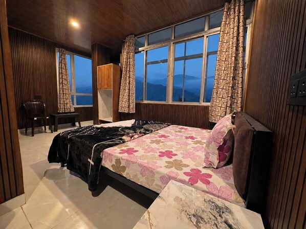 A bedroom with a bed, a chair, a desk, and a view of the mountains through the window.