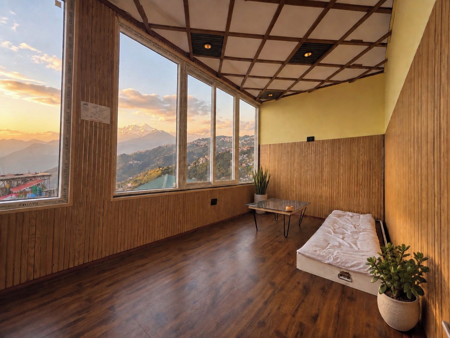 A room with a wooden floor, a bed, a small table, and a potted plant.