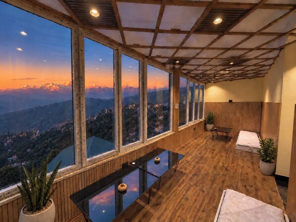 A room with a large window overlooking a mountainous landscape, a wooden floor, a small table with a vase, and a bench with a towel.